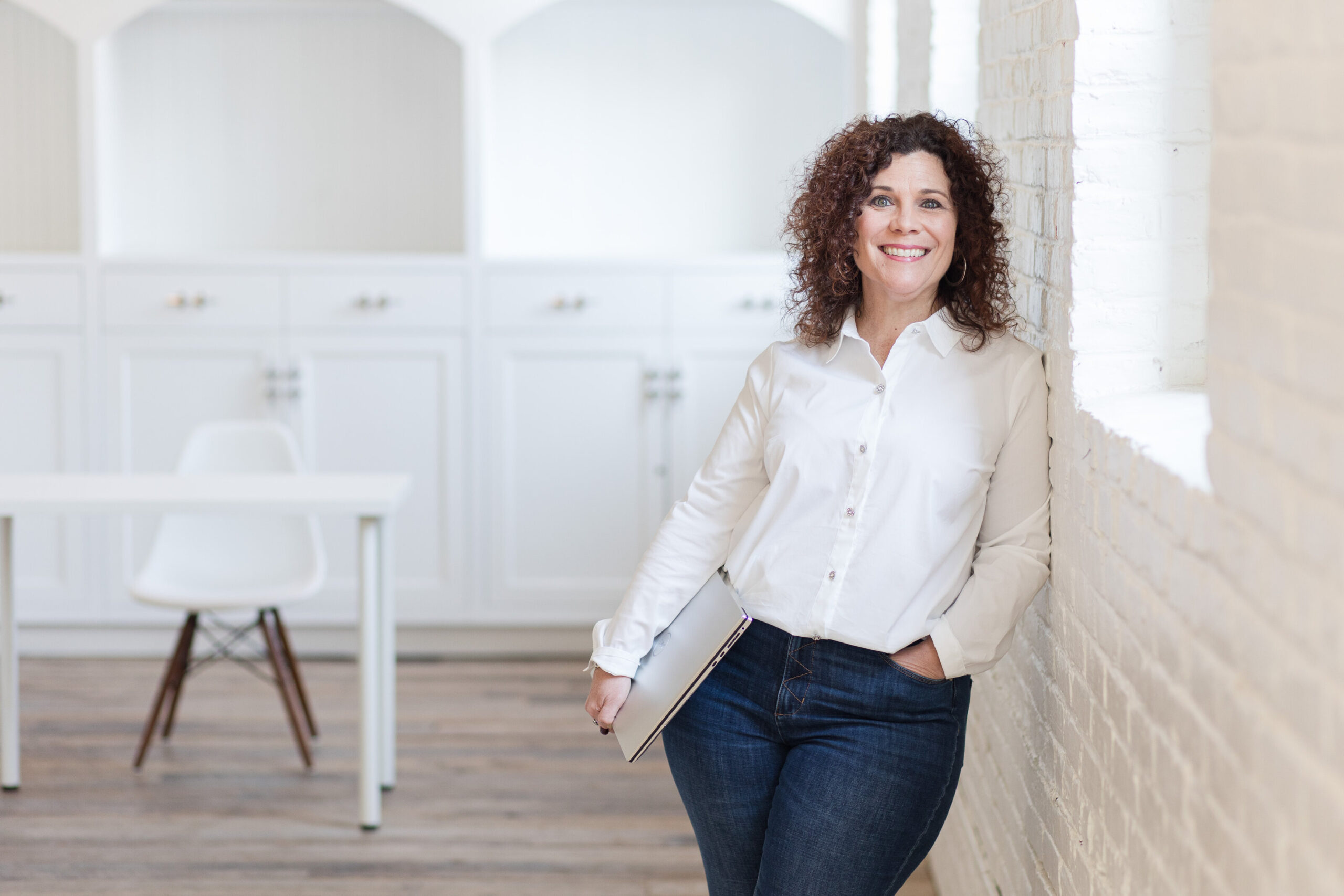 Theresa in a white blouse leaving against a white brick wall in a studio